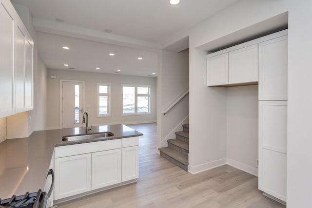 kitchen with a sink, light wood-style floors, white cabinetry, and a peninsula