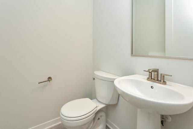half bath featuring toilet, baseboards, and a sink