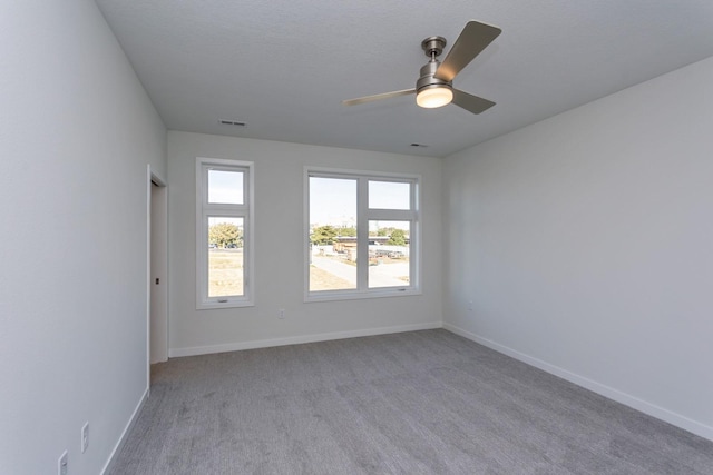 carpeted spare room with baseboards, a ceiling fan, and visible vents