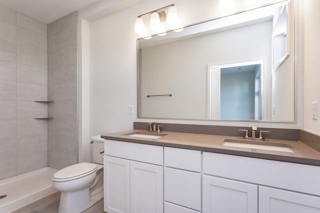 bathroom with toilet, double vanity, a sink, and a tile shower