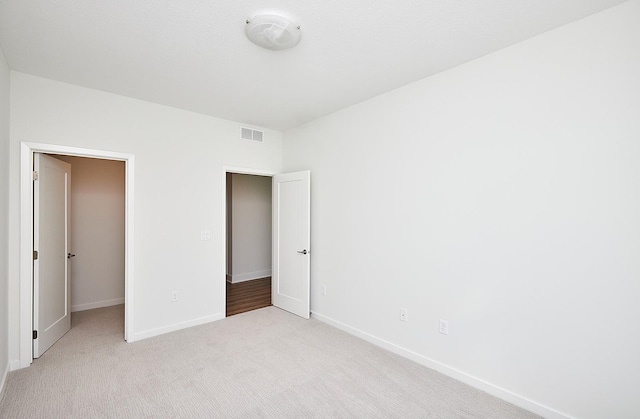 unfurnished bedroom with a spacious closet, visible vents, baseboards, and light colored carpet