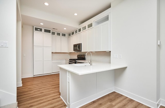 kitchen with a sink, decorative backsplash, light wood-style floors, a peninsula, and appliances with stainless steel finishes