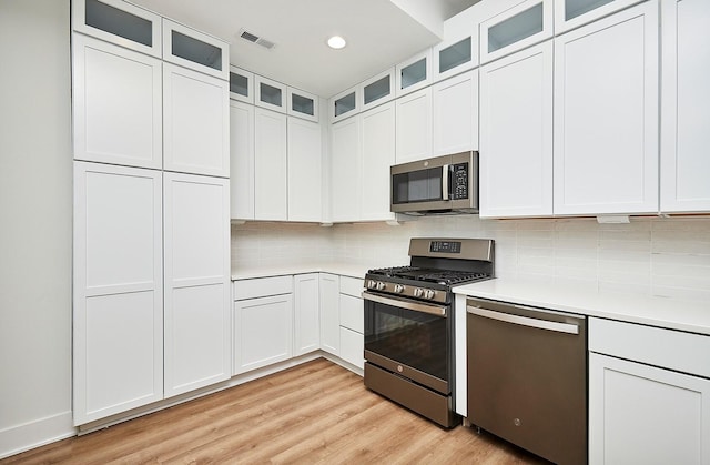 kitchen featuring light wood finished floors, stainless steel appliances, light countertops, visible vents, and tasteful backsplash