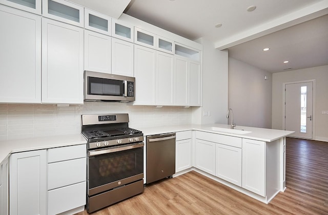 kitchen with a sink, light wood-type flooring, a peninsula, tasteful backsplash, and appliances with stainless steel finishes