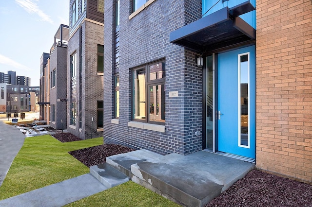 doorway to property featuring brick siding and a lawn