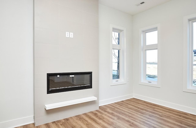 unfurnished living room featuring wood finished floors, baseboards, a large fireplace, and visible vents