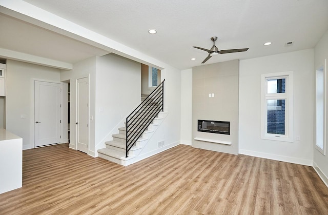 unfurnished living room featuring a ceiling fan, light wood-style floors, a fireplace, recessed lighting, and stairs