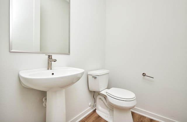 half bathroom featuring toilet, wood finished floors, a sink, and baseboards