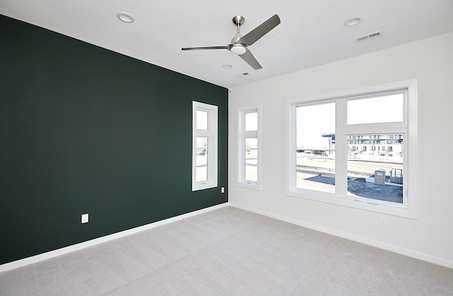 empty room with light carpet, visible vents, ceiling fan, and plenty of natural light