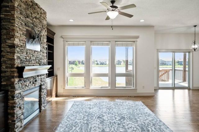 2102 NW 24th St, Ankeny, IA 50023 - unfurnished living room with a textured ceiling, ceiling fan, a stone fireplace, wood finished floors, and a water view