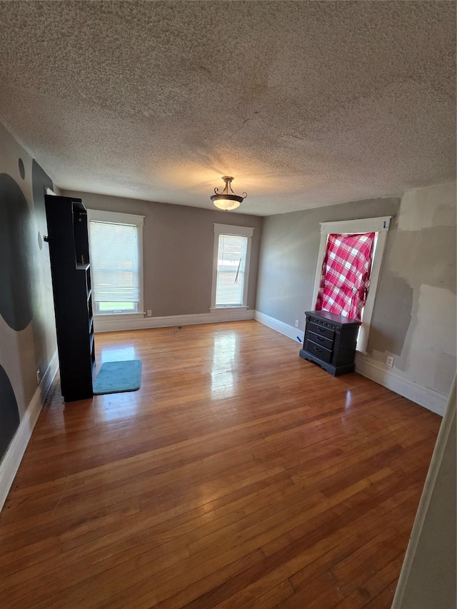 unfurnished living room with a textured ceiling, wood finished floors, and baseboards
