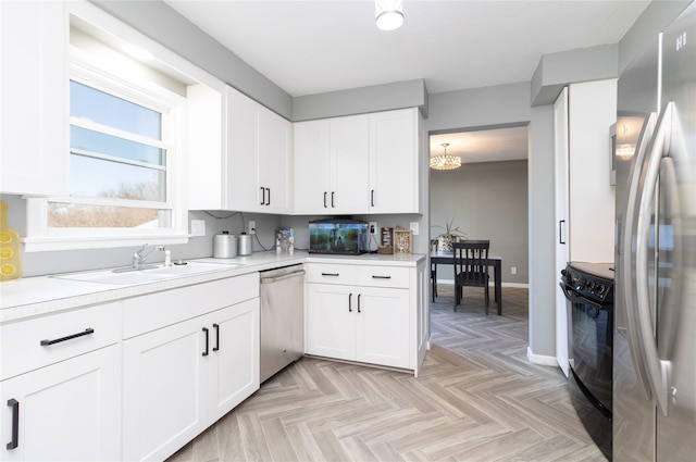 kitchen with white cabinets, appliances with stainless steel finishes, a sink, light countertops, and baseboards