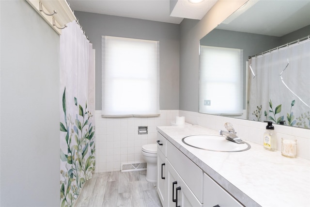 bathroom featuring vanity, a wainscoted wall, toilet, visible vents, and tile walls