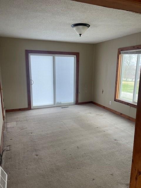 unfurnished room featuring visible vents, light colored carpet, baseboards, and a textured ceiling
