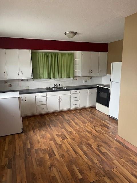 kitchen with range with electric stovetop, dark countertops, freestanding refrigerator, dark wood finished floors, and decorative backsplash