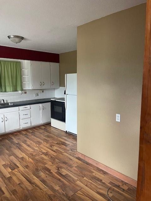 kitchen with freestanding refrigerator, tasteful backsplash, dark countertops, electric stove, and dark wood-style floors