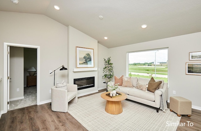 living area featuring lofted ceiling, a glass covered fireplace, wood finished floors, and baseboards