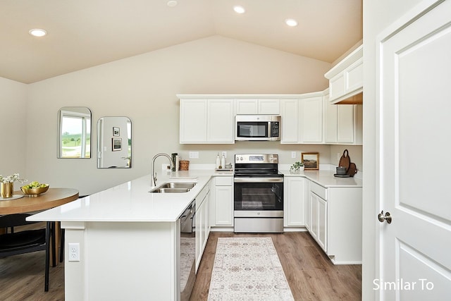 kitchen with a peninsula, a sink, vaulted ceiling, wood finished floors, and appliances with stainless steel finishes