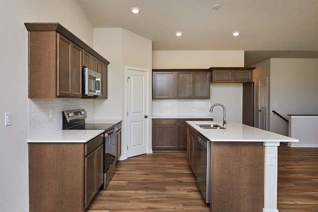 1139 NW Petersen Dr, Waukee, IA 50263 - kitchen featuring appliances with stainless steel finishes, dark wood finished floors, decorative backsplash, a kitchen island with sink, and recessed lighting