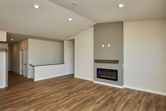 1139 NW Petersen Dr, Waukee, IA 50263 - unfurnished living room featuring wood finished floors, lofted ceiling, a glass covered fireplace, a textured ceiling, and recessed lighting