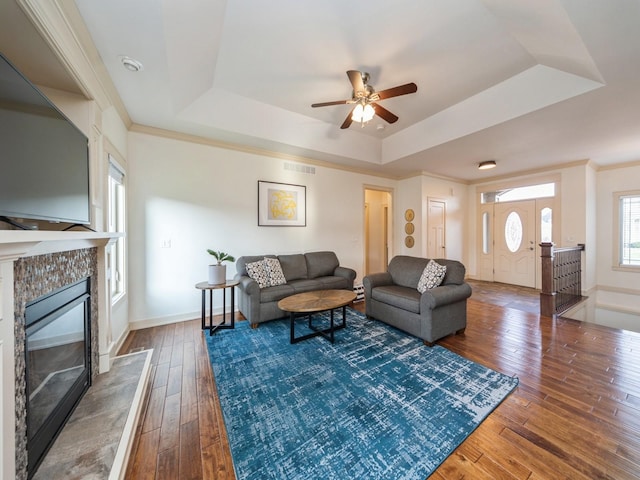living area featuring hardwood / wood-style floors, a tray ceiling, visible vents, a tiled fireplace, and ceiling fan
