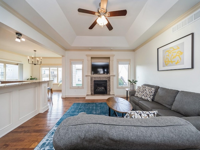 living area with ceiling fan with notable chandelier, a fireplace, dark wood finished floors, visible vents, and a raised ceiling