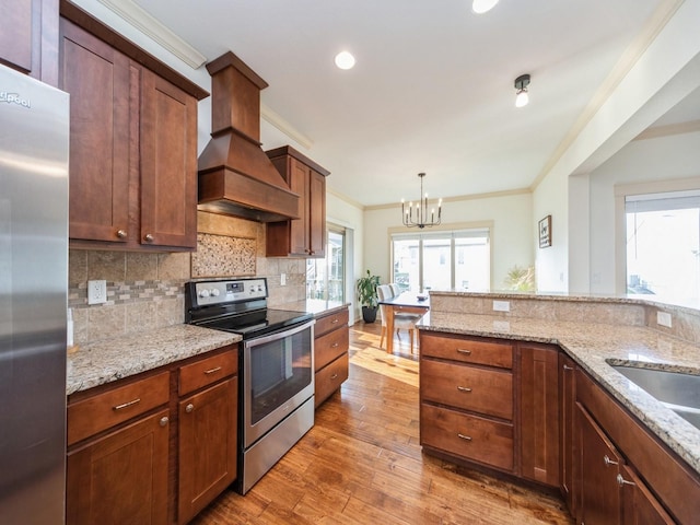kitchen featuring stainless steel appliances, ornamental molding, light wood-style flooring, a notable chandelier, and custom range hood