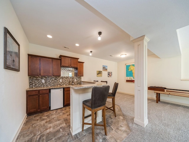 kitchen featuring a breakfast bar, dishwasher, light stone countertops, baseboards, and tasteful backsplash