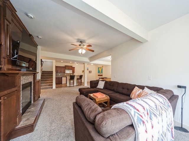 living room featuring a glass covered fireplace, a ceiling fan, and light carpet