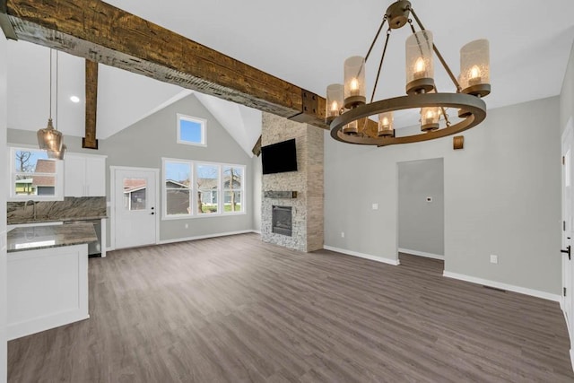 unfurnished living room featuring a sink, baseboards, an inviting chandelier, beamed ceiling, and wood finished floors