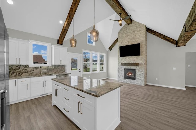 kitchen with dark stone countertops, wood finished floors, a sink, open floor plan, and beamed ceiling