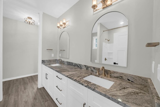 full bath with an inviting chandelier, wood finished floors, a sink, and double vanity