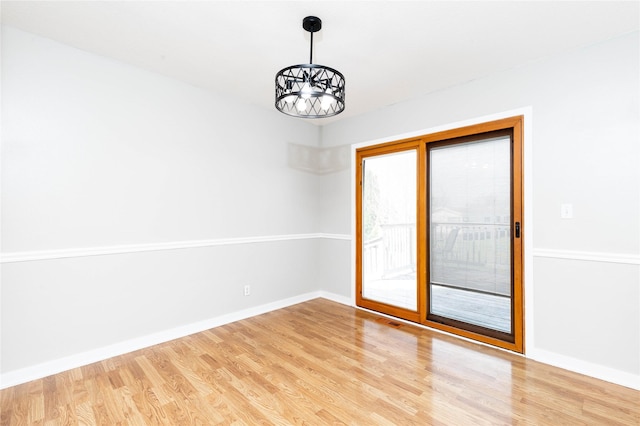 empty room with light wood-type flooring, baseboards, and a notable chandelier