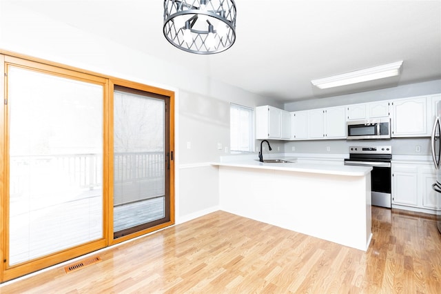 kitchen featuring stainless steel appliances, light wood-style flooring, a sink, white cabinetry, and light countertops