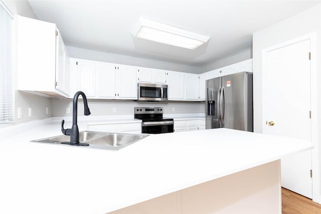 kitchen with a sink, stainless steel appliances, light countertops, white cabinets, and a peninsula