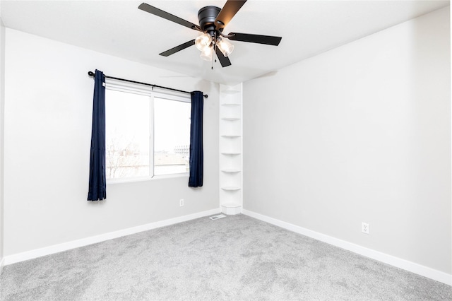 empty room with carpet, visible vents, a ceiling fan, and baseboards