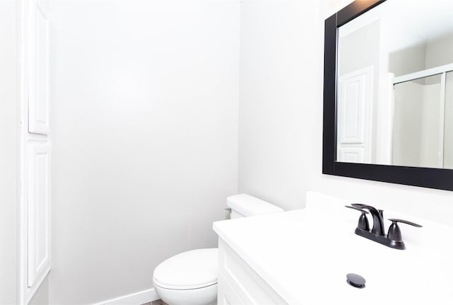 bathroom with toilet, a shower with door, vanity, and baseboards