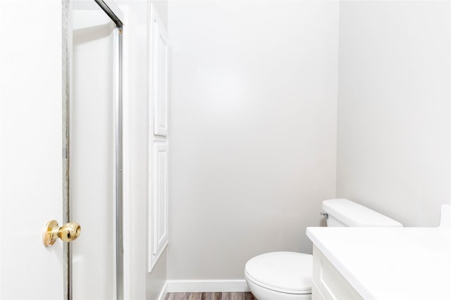 bathroom with toilet, vanity, wood finished floors, and baseboards