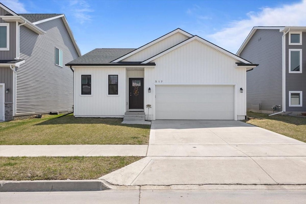 view of front of property featuring a shingled roof, a front lawn, entry steps, an attached garage, and driveway