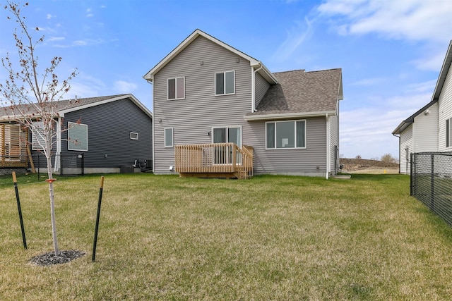 rear view of property with a lawn, a wooden deck, fence, and a shingled roof
