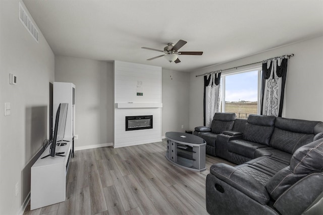 living room with a ceiling fan, light wood-type flooring, a large fireplace, baseboards, and visible vents