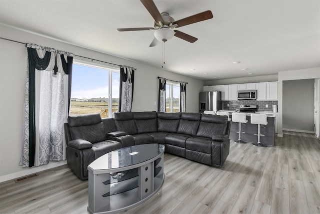living area featuring light wood-type flooring, a ceiling fan, and visible vents