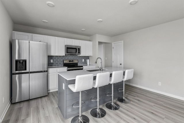 kitchen featuring an island with sink, light wood-style floors, stainless steel appliances, white cabinets, and baseboards