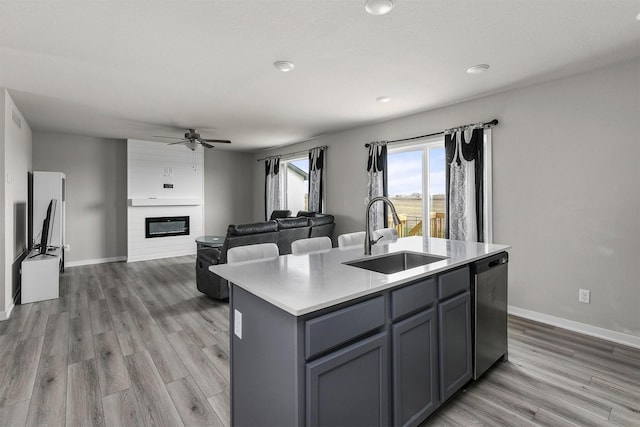 kitchen featuring stainless steel dishwasher, a ceiling fan, a sink, a kitchen island with sink, and light countertops
