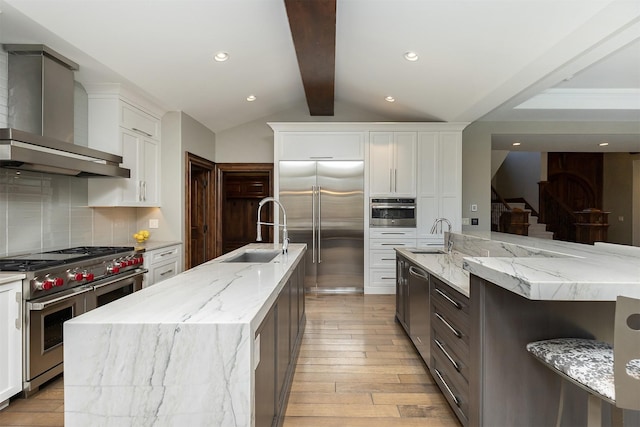kitchen featuring a spacious island, wall chimney range hood, high quality appliances, and a sink