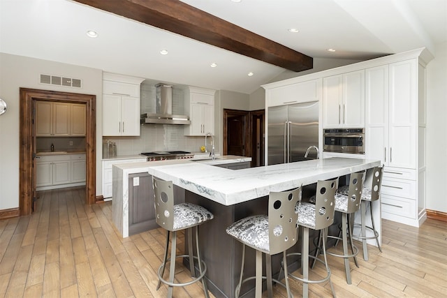 kitchen featuring wall chimney range hood, decorative backsplash, a spacious island, appliances with stainless steel finishes, and visible vents