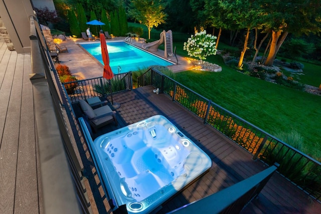 view of swimming pool featuring a fenced in pool, a water slide, a yard, a wooden deck, and hot tub deck surround