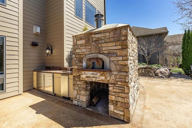 view of patio / terrace with an outdoor stone fireplace, an outdoor kitchen, and fence