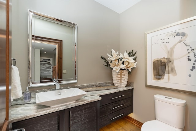 half bath with toilet, vanity, and wood finished floors
