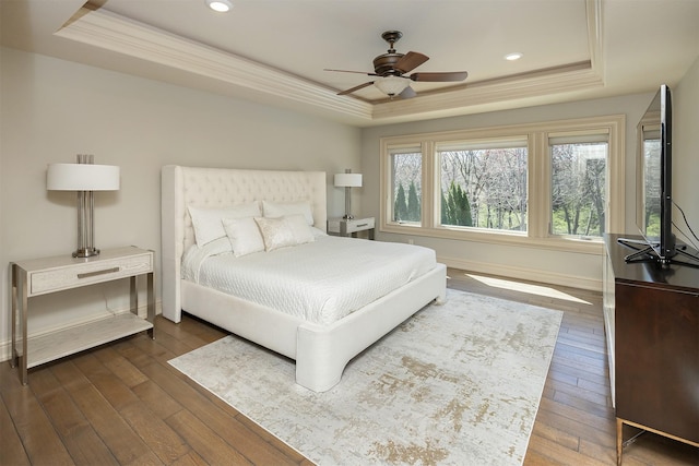bedroom with a tray ceiling, dark wood-style floors, baseboards, recessed lighting, and crown molding